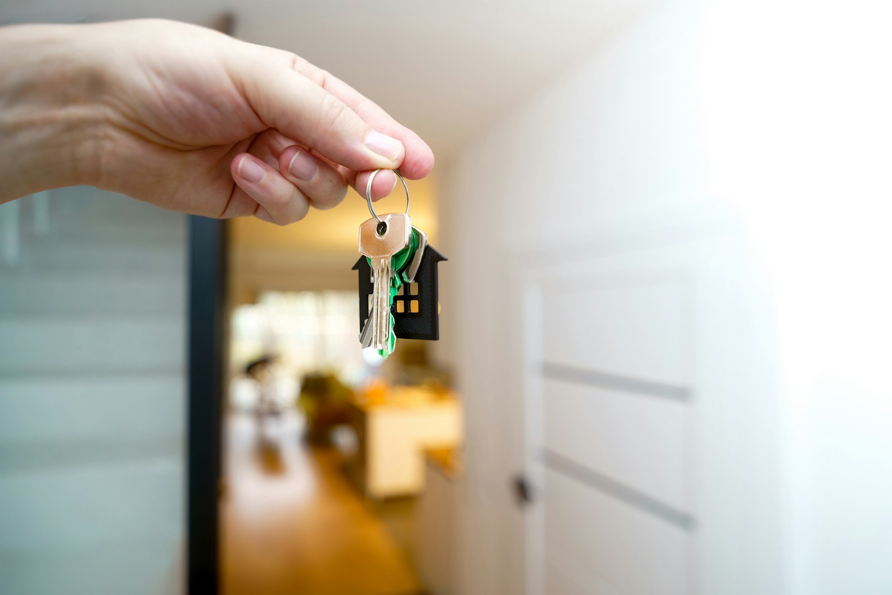 main qui tend un trousseau de clés en forme de maison devant la porte d'un logement