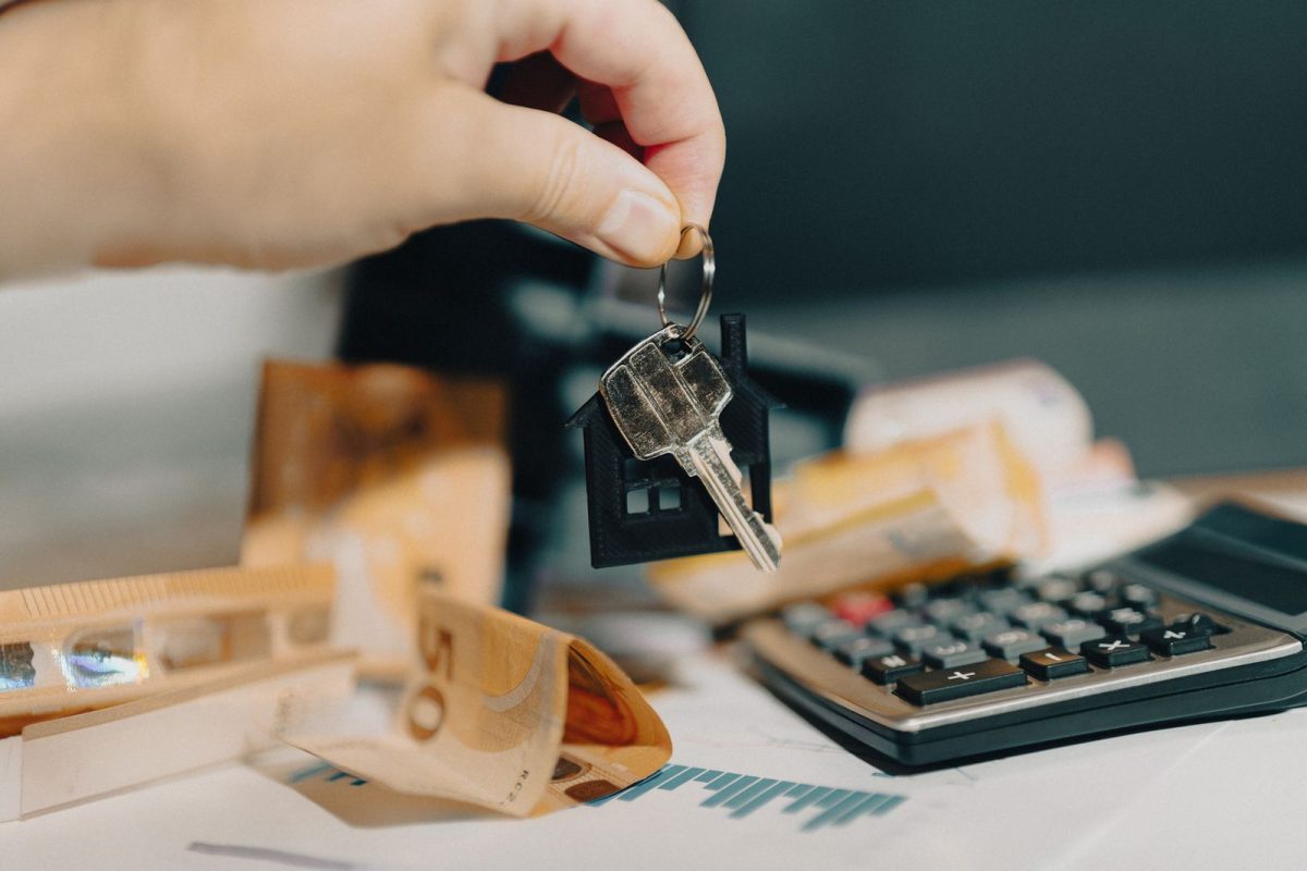 mains tenant des cles en forme de maison avec des billets et une calculatrice