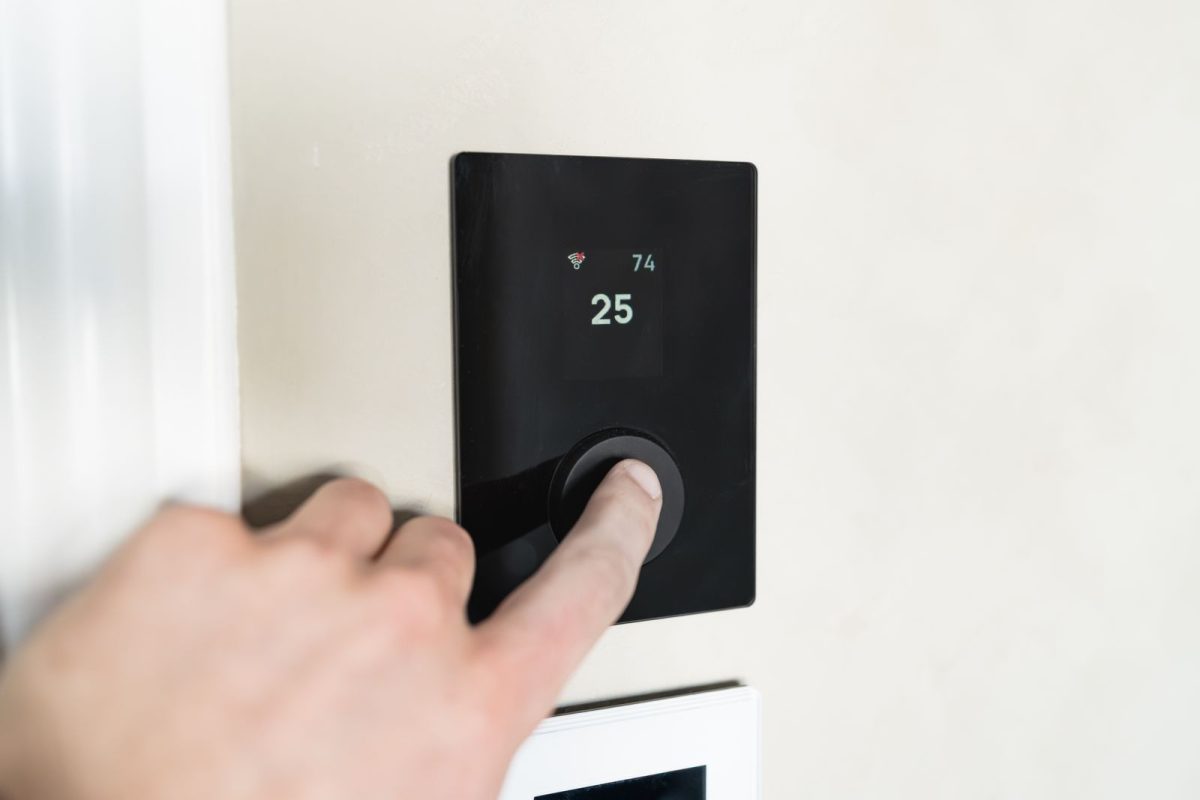 Main qui regle un thermostat connecte moderne fixe au mur