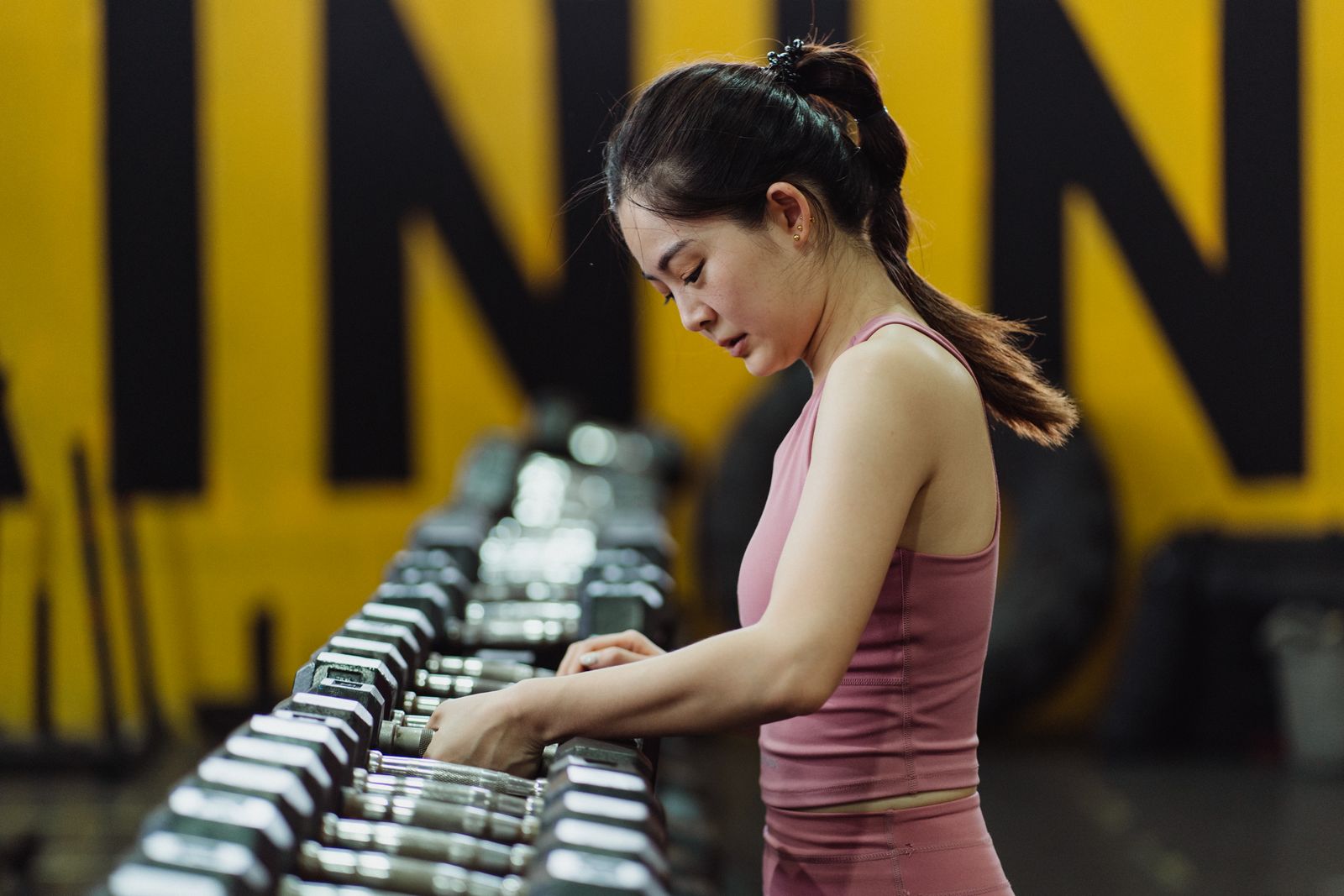 Femme qui choisit un haltère dans la zone musculation d'une salle de sport